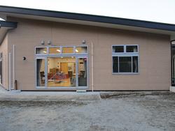 大きなガラス扉と窓から室内の明かりが見え、椅子やテーブルが配置された様子がうかがえる平屋の戸倉地区放課後児童クラブの写真