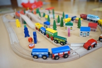 木製の線路の上を走るカラフルな機関車、周囲には木や家、車などが配置されたおもちゃの街の風景を捉えた写真