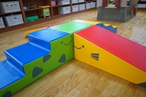 鮮やかな青、緑、赤、黄色のソフトな素材でできた積み木が組み合わさり、階段や坂道になっている子供用の遊具の写真
