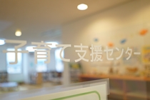 「子育て支援センター」という文字がガラス戸に描かれており、その奥に明るく整頓された部屋がぼんやりと見える室内の写真
