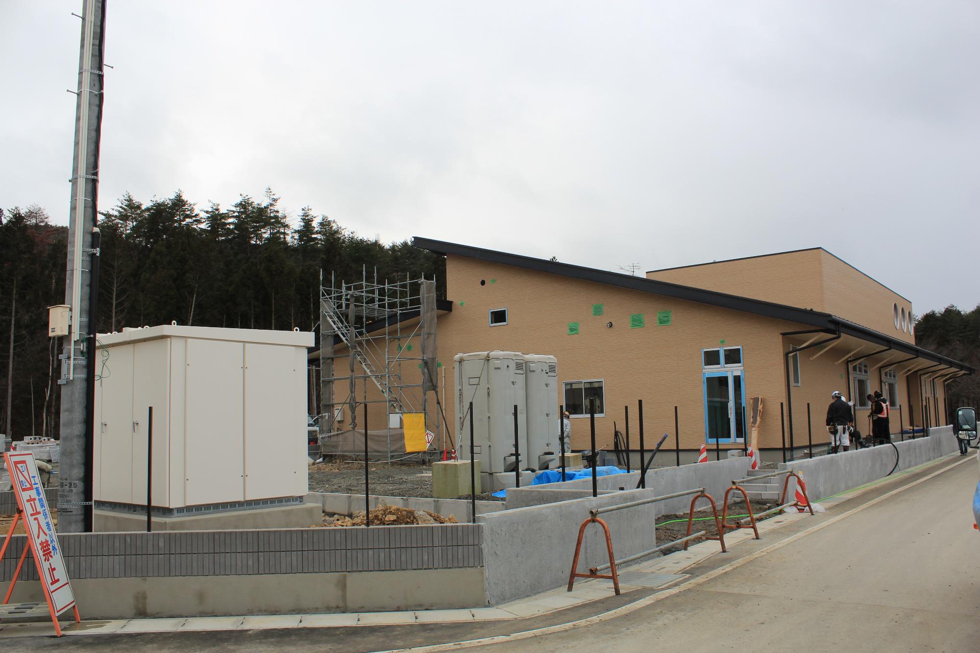 ベージュ色の外壁で平屋建ての戸倉地区子育て支援拠点施設の周りの外構工事が進められている写真