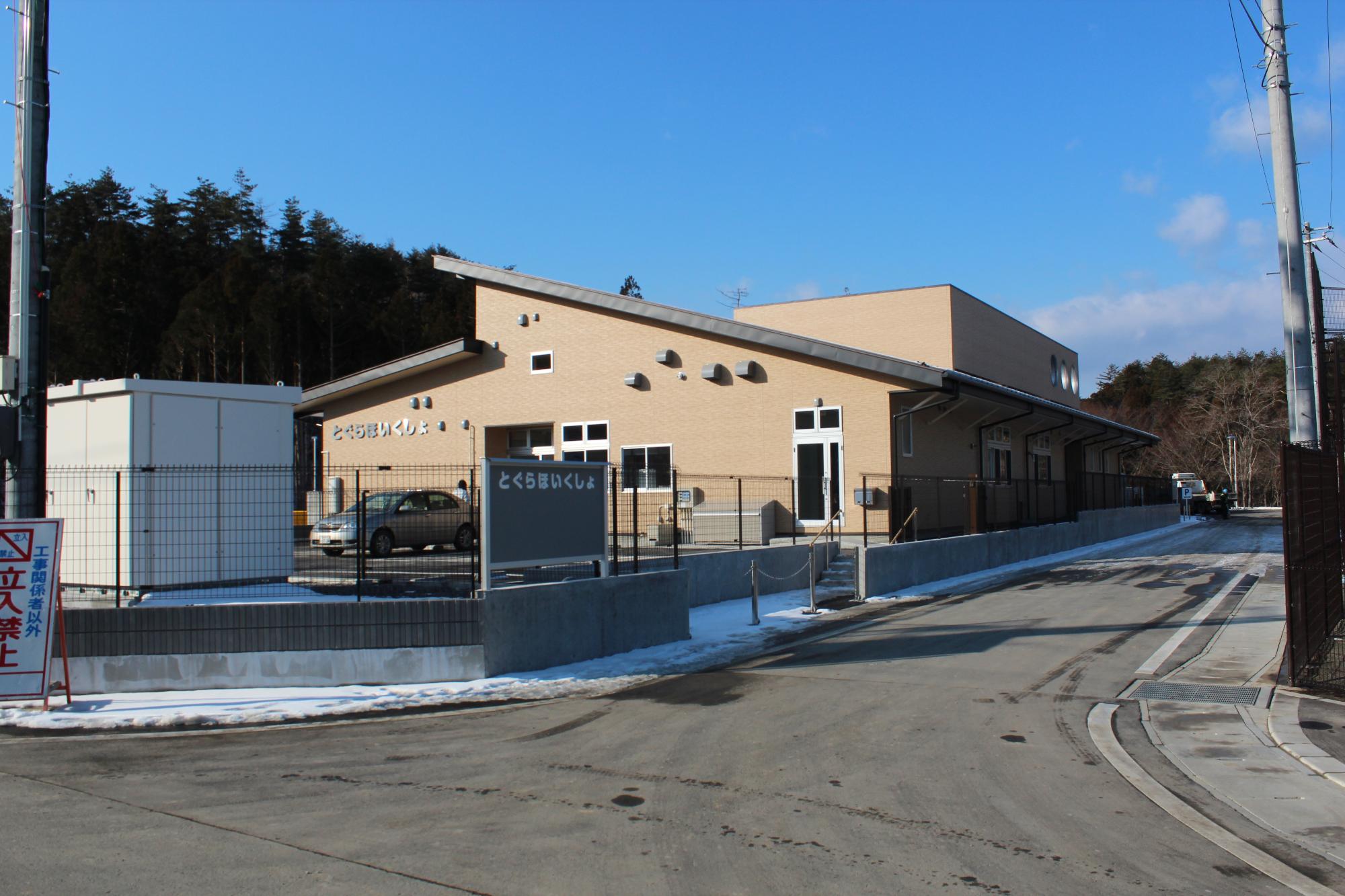 建物周りにフェンスが設置され、フェンスの一部に「とぐらほいくしょ」の看板が設置された写真