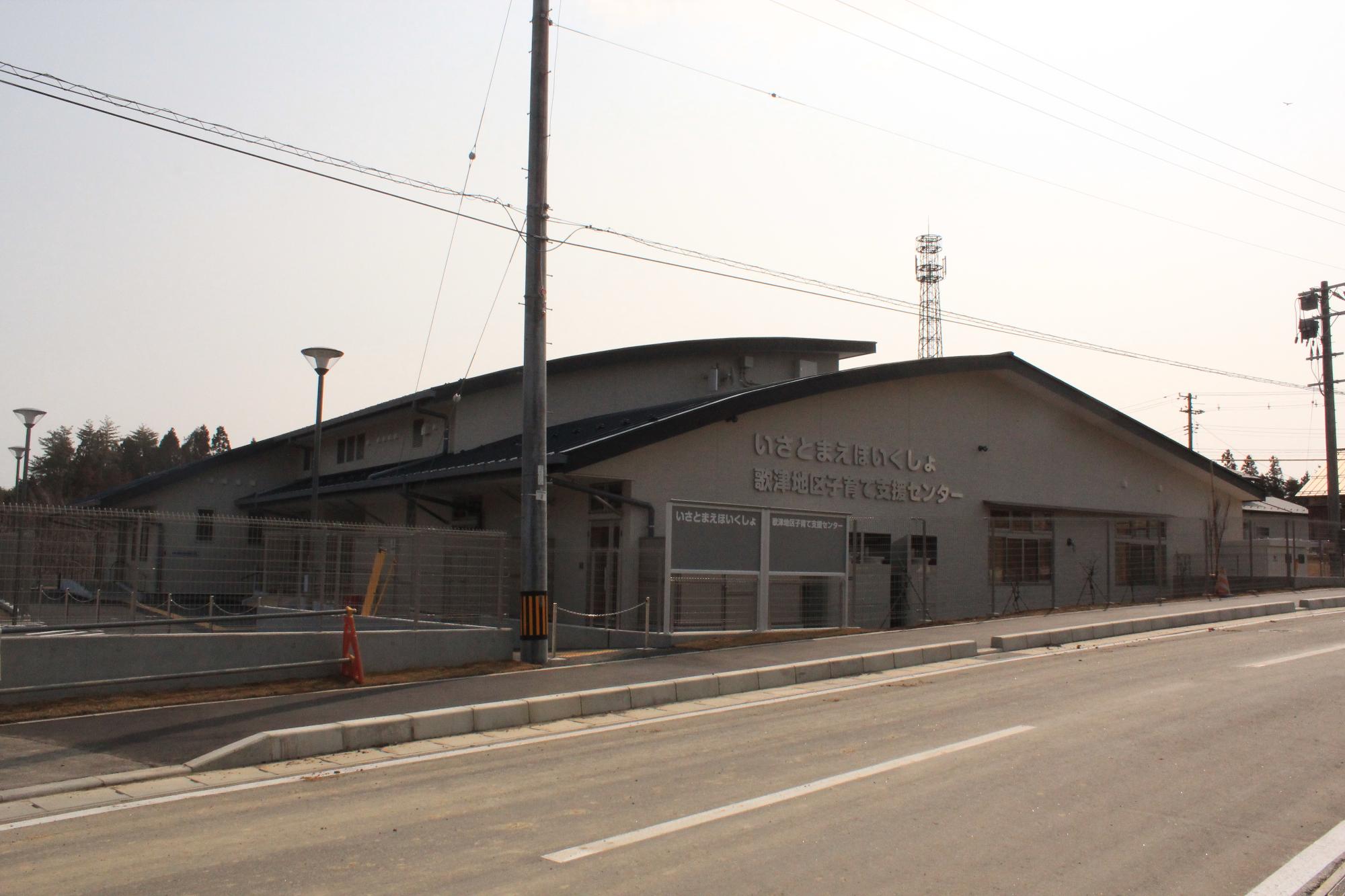 「いさとまえほいくしょ 歌津地区子育て支援センター」と書かれた看板が掲げられた平屋建ての建物が、舗装された道路沿いに建っている写真