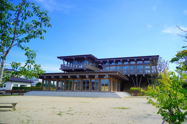木造で大きな窓が並ぶ2階建ての建物が木々が植えられた広い砂の敷地に建っている、あさひ幼稚園の外観写真