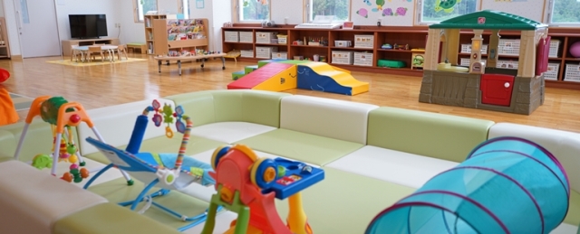 子供向け遊具やカラフルな滑り台、おもちゃなどが整然と配置された、木製の床が清潔な広いプレイルームの写真