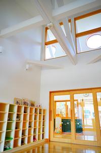 棚にたくさんの靴が並び、高い天井に白い梁と窓があり明るい光が差し込むエントランスホールの写真