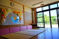 大きな窓から自然光が差し込む保育室の一部に畳が敷かれ、壁には鳥とリスのキャラクターとカラフルな飾りがあしらわれた装飾が掲げられている写真