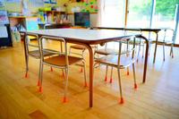 5脚の小さな椅子と机が並び、窓から光が差し込む明るい保育室の写真