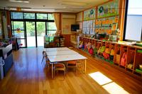 明るい日差しが差し込む保育室内に、子どもたちの荷物が整然と並んだ棚や小さな机と椅子が配置され、壁には季節の制作物や作品が飾られている写真
