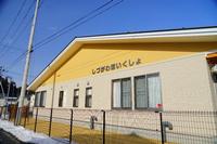 黄色の外壁に「しづかわほいくしょ」と書かれた看板がある園舎の外観を、雪が少し残る道路側から撮影した写真