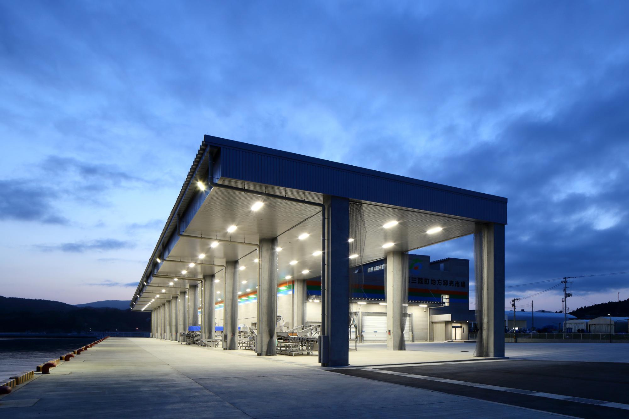 雲がかかった薄暗い空を背景に照明が灯った市場の外観を下から見上げるように撮影した写真