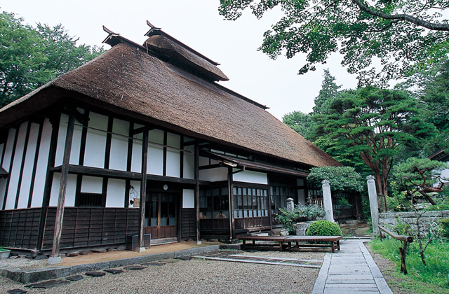 木々に囲まれた藁葺き屋根の建物で周りに砂利がしかれている松笠屋敷の外観写真