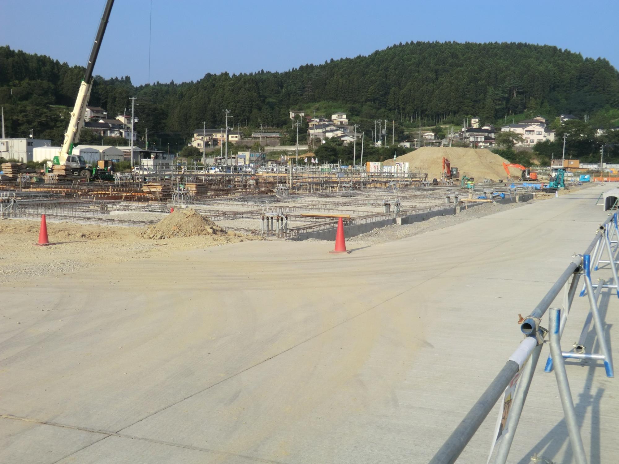 鉄筋が組まれた基礎部分とクレーン車が稼働する、コーンやフェンスで囲まれ安全対策が施された建設中の工事現場の写真