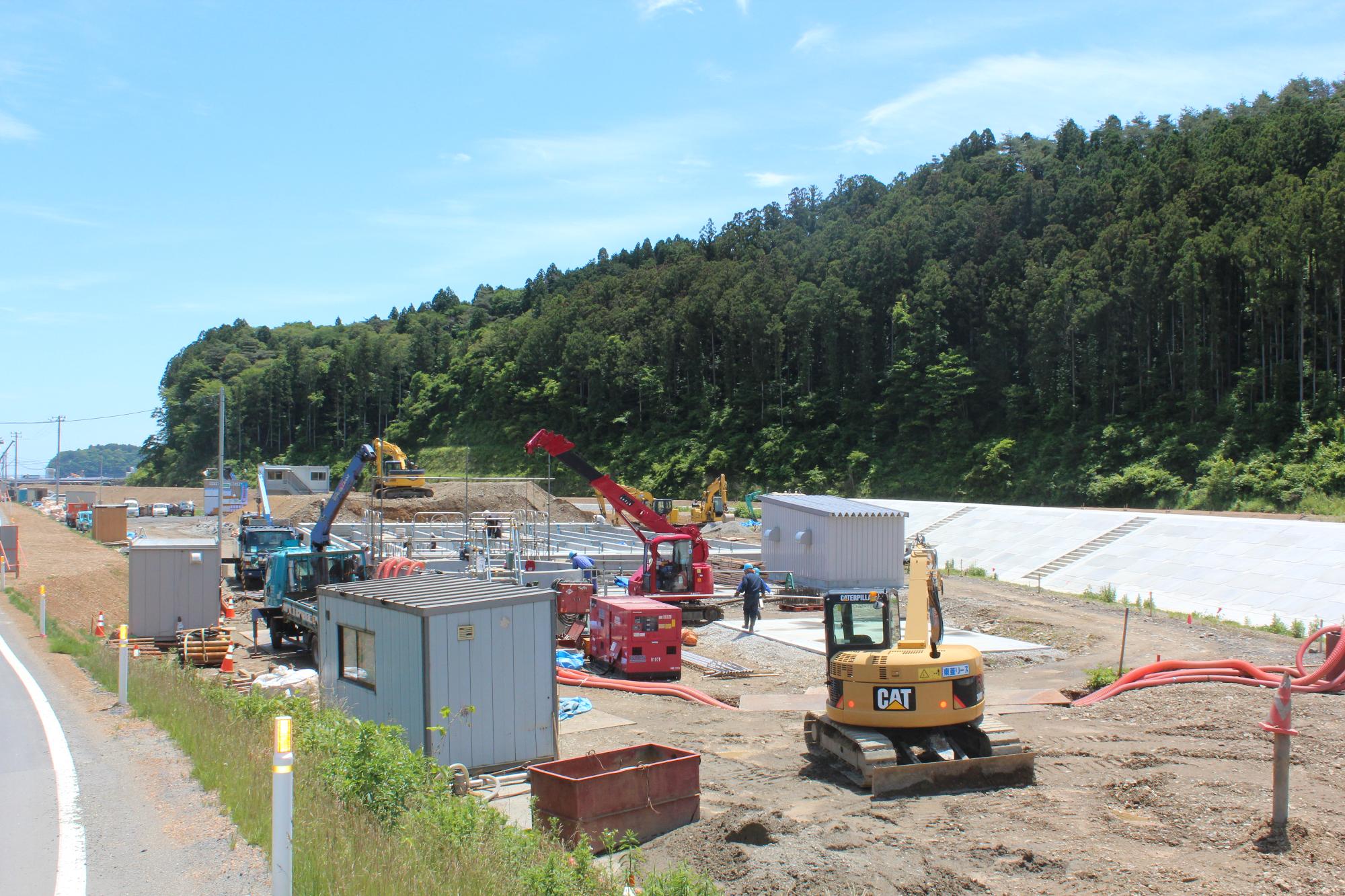 造成地で大型クレーンやショベルカーが稼働し、仮設小屋や資材が配置され、コンクリート基盤や盛土が整備される様子を撮影した水尻ふ化場の建設中写真