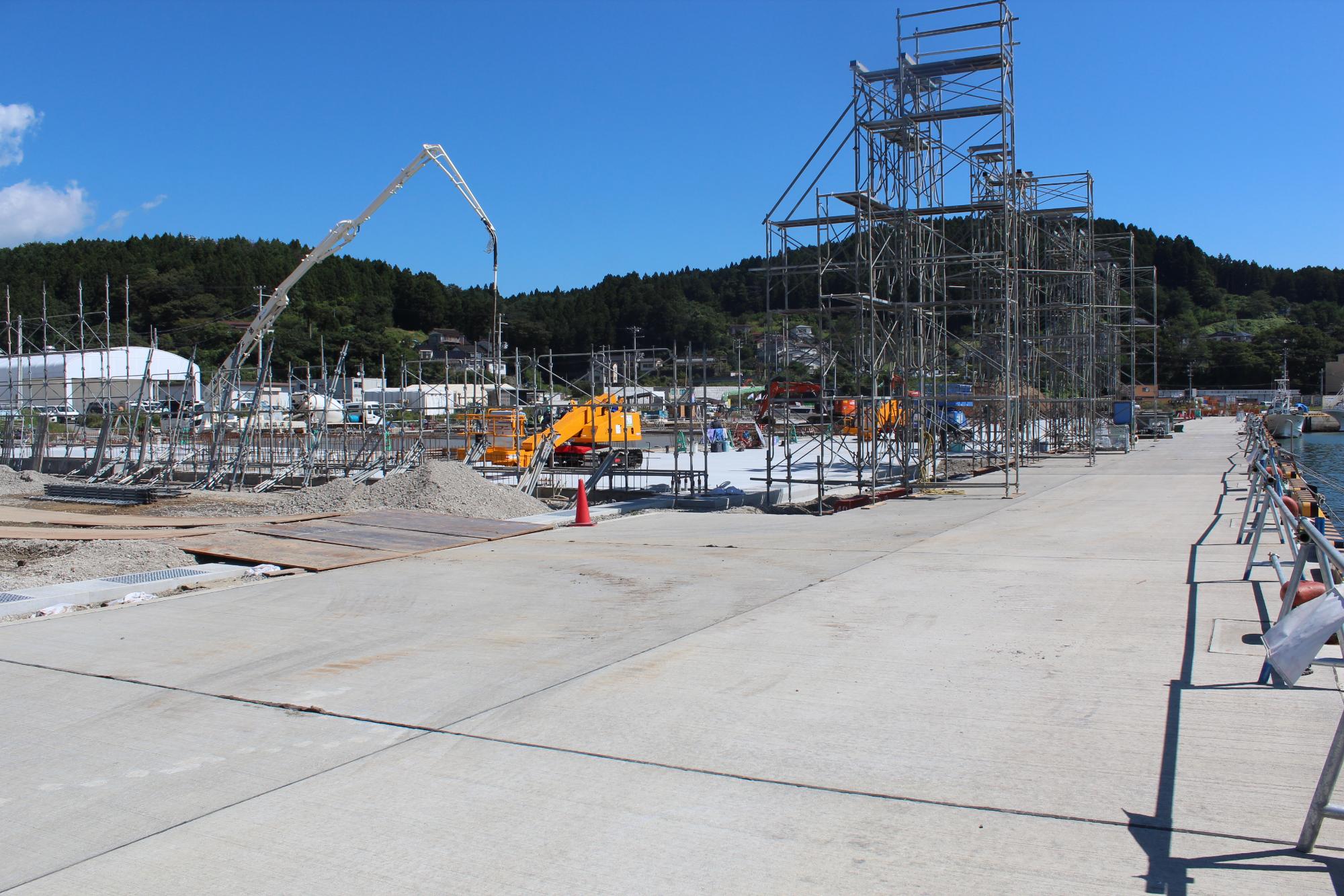 鉄骨の足場やクレーン、コンクリートポンプ車が配置された、建設中の工事現場の写真