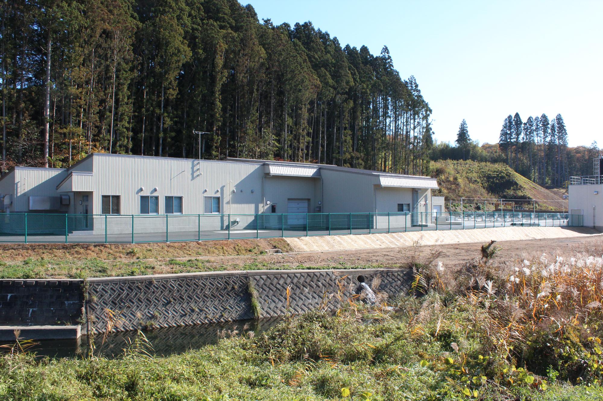 川沿いに建つ灰色の平屋建て施設の小森ふ化場の外観写真