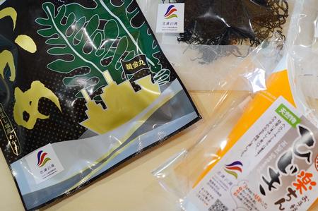 黄金丸と書かれた大漁旗が掲げられた金色をした漁船のシルエットとワカメのイラストが描かれた商品パッケージと「楽ちんひじき」と中央に印字された商品パッケージが置かれている写真