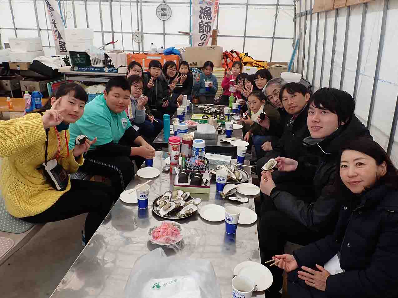 テーブルを囲んだ子供たちがカメラに向かってピースサインをしているバーベキューの様子の写真