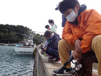 岸壁に座って釣りをしている子どもたちの写真