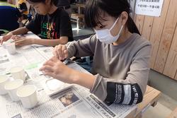 新聞紙の上で女の子が石膏をアンモナイトの型に流し込んでいるレプリカ作り体験の様子の写真
