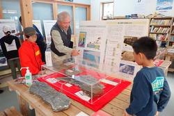 博物館の展示ケースを囲んで男性講師の説明を聞く子どもたちの写真