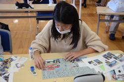 机の上に並べた写真や文章を貼り付けてポスターを作っている女の子の写真