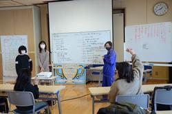 ホワイトボードの前で先生の話を聞きながら手を挙げている子どもたちの写真