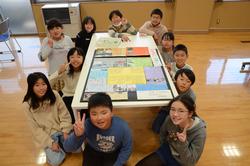 完成したカラフルなポスターを囲んで笑顔でポーズをとっている子どもたちの写真