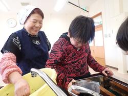 年配の女性と一緒に、子どもが大きな桶の中で海苔作りをしながら笑顔で交流している写真
