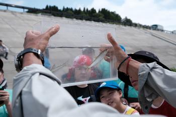 男性が持った透明な容器に入れた採れた魚を子供たちが観察している写真