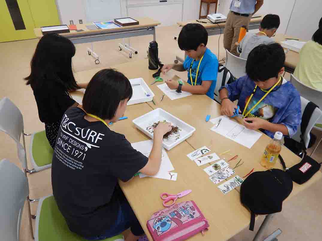 机を囲んで座った子どもたちが、はさみや紙を使って工作に集中している様子が写っている写真