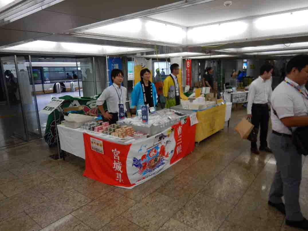 複数の男性が屋内の展示スペースの一角で商品を販売している様子を写した写真