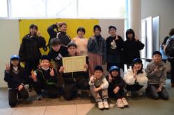 賞状を持った男の周りに集まった子どもたちが笑顔で写っている集合写真