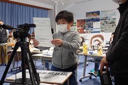 カメラの前で紙を読み上げている子どもの写真