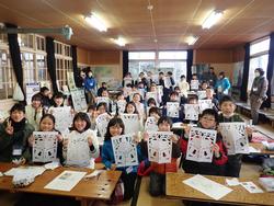 広い和室の部屋で、ハサミで切り絵をしたきりこの紙を手に持ち、カメラに向かってポーズをとっているたくさんの子どもたちの写真