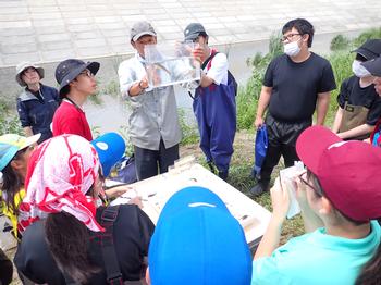 男性が持つ小さな透明の水槽の中に入った生物を、集まった参加者たちが見ている写真