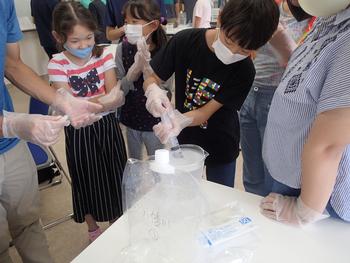 室内で両手にビニールの手袋を付けてろ過作業を行っている子どもたちの写真