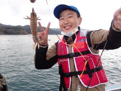 小さな魚を釣ってカメラに向かって笑顔でピースサインをしている男の子の写真