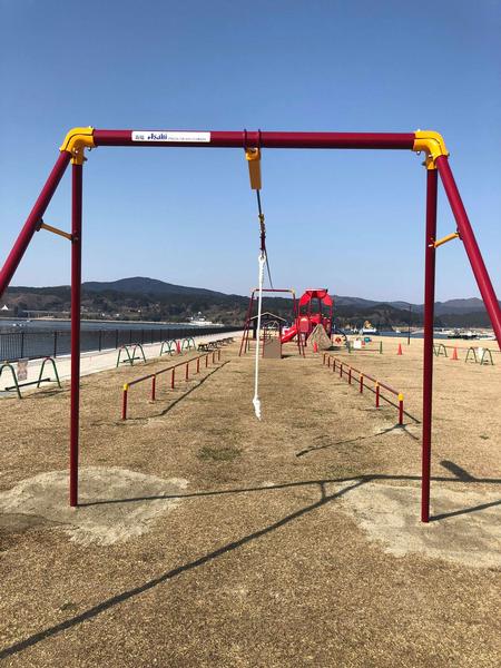 海沿いの広い公園の中に、赤と黄色のジップライン遊具が設置されている写真