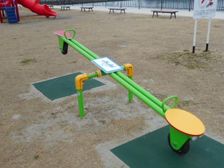 緑と黄色の配色のカラフルなシーソーが公園の広場に設置されている写真
